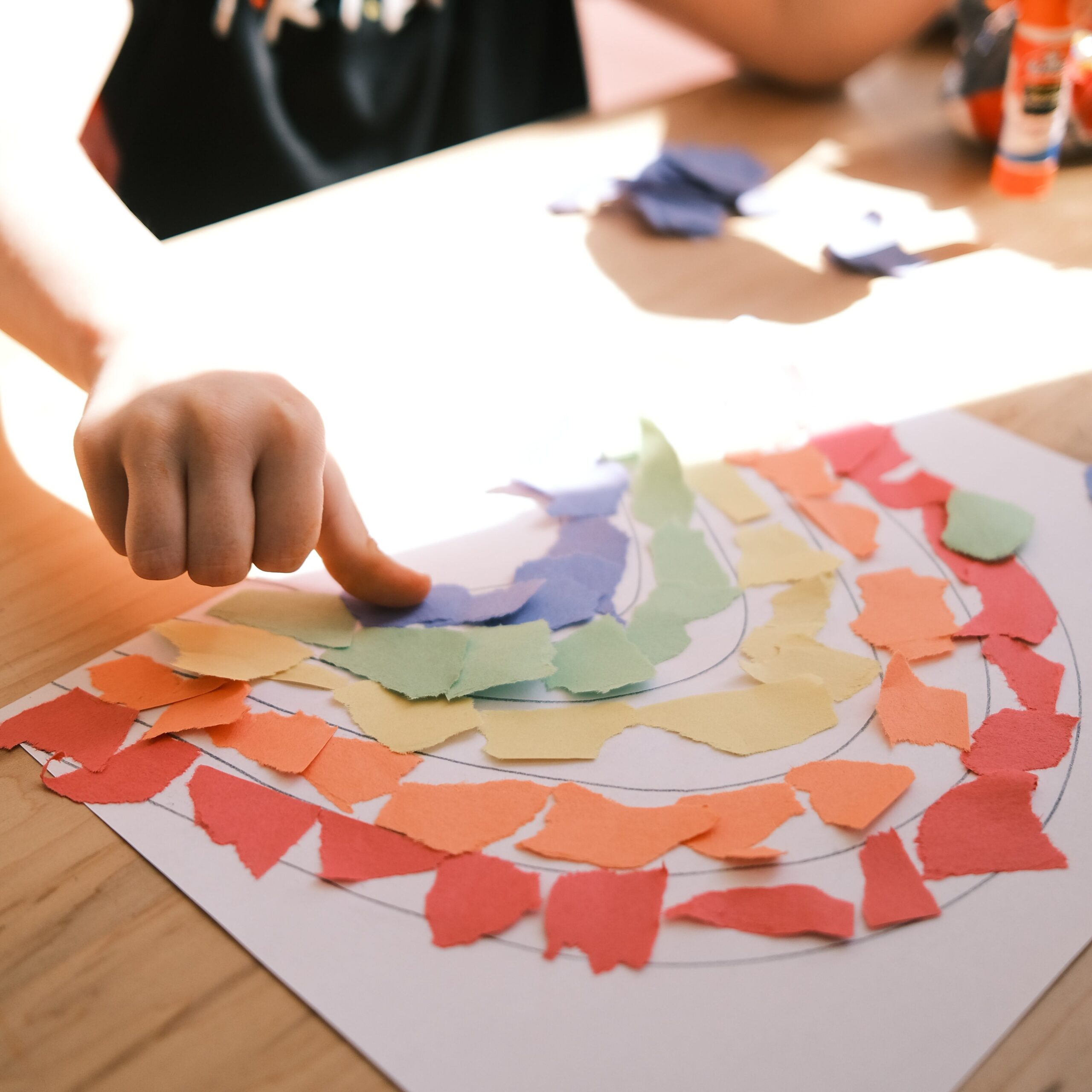 A child makes a rainbow craft out of torn, colored construction paper.