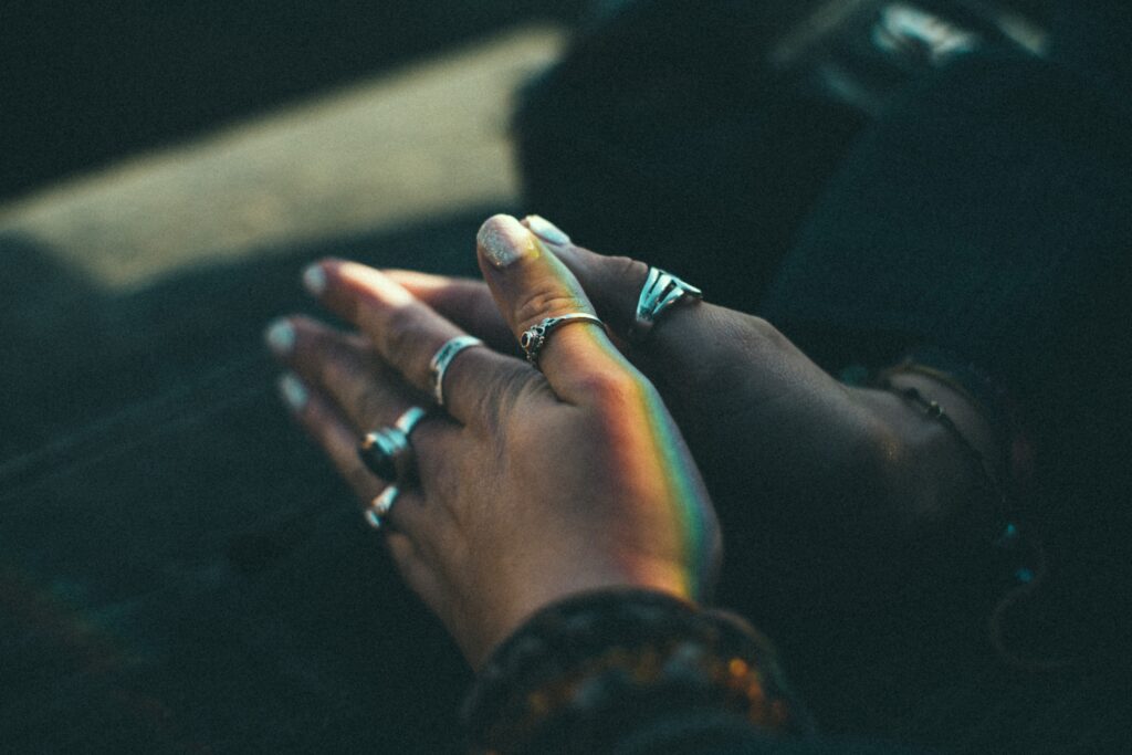 Decorative. Hands join together in prayer. A light reflection on one hand creates a rainbow.