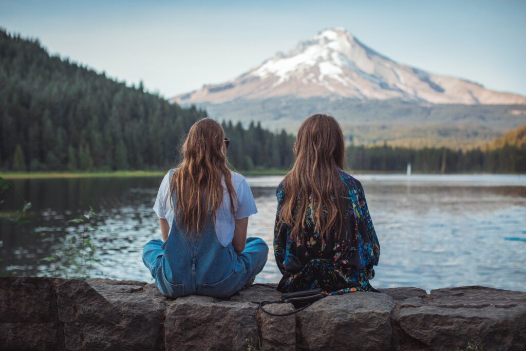Decorative. Two young people with long hair sit together looking at a mountain in the distance. Their bodies are not touching.