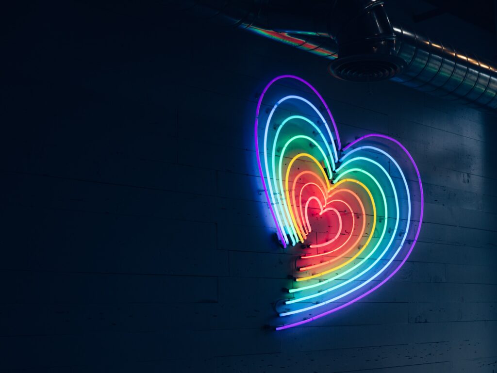 Decorative. A neon light sign includes rainbow colored lines in the shape of a heart.