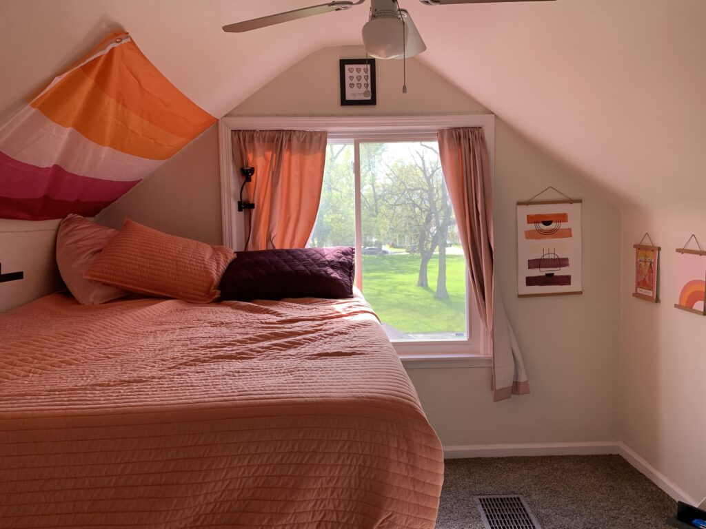 A bedroom has orange, pink, and purple decor. A lesbian flag hangs on the wall.
